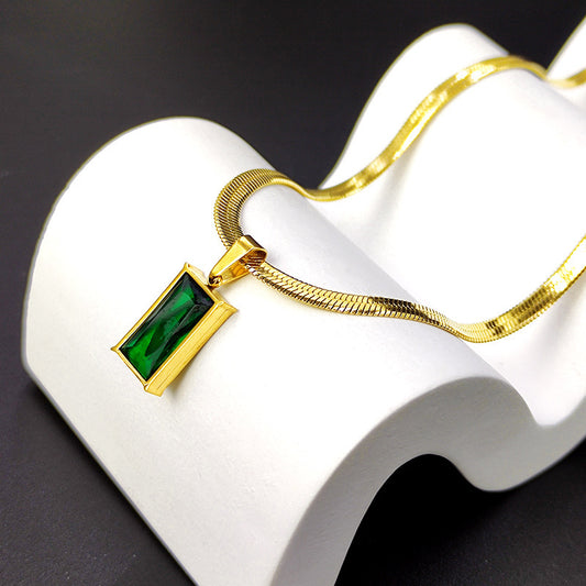 Gold necklace with a green gemstone pendant on a white stand against a black background