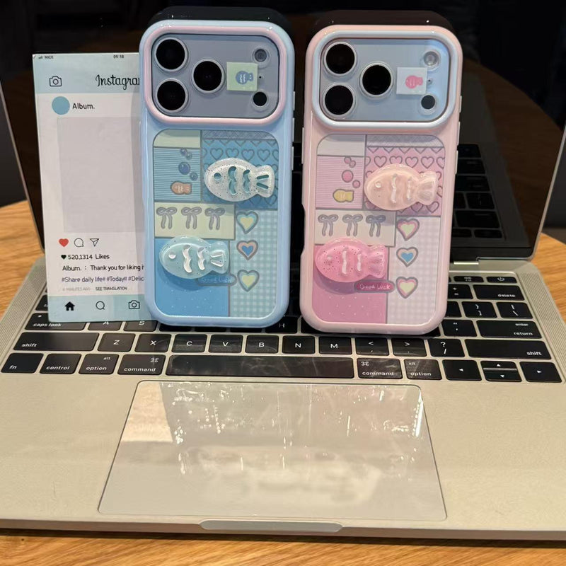 Dual iPhone case pair on laptop: pale blue and pink with hearts and raised fish