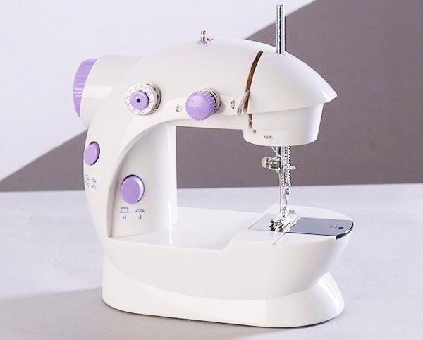 Miniature white sewing machine with purple controls and needle over base