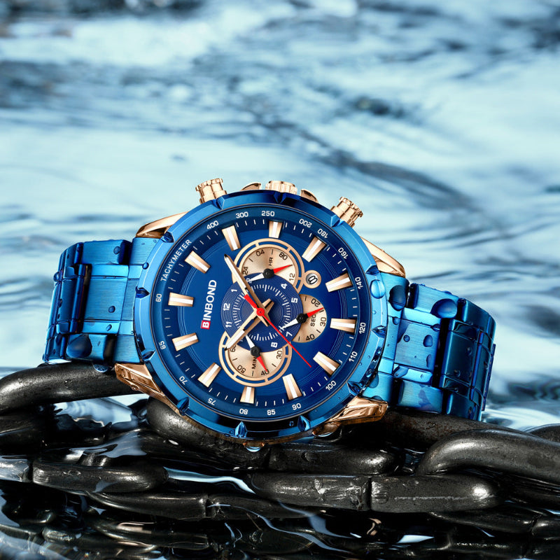 Blue dial tactical wristwatch with gold bezel and blue metal bracelet on dark stones