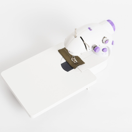 Mini sewing machine stitching olive fabric with needle and presser foot