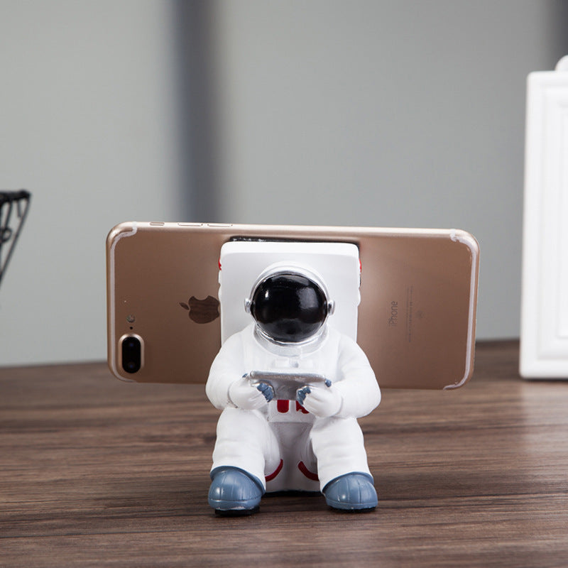 Astronaut mobile phone stand holding a phone horizontally, white suit and blue shoes