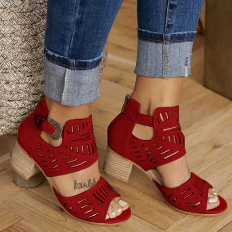 Red open-toe sandals with cut-out design worn with rolled-up jeans on a wooden floor.