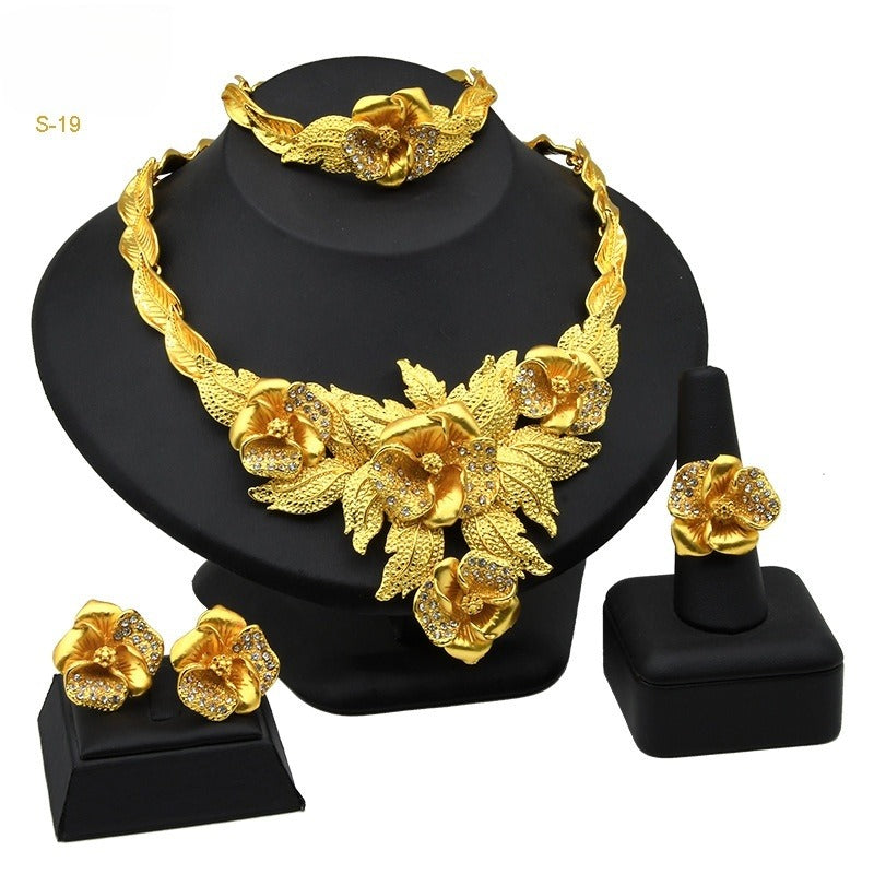 Gold-tone four-piece jewelry set with floral choker necklace, matching earrings, bracelet, and ring