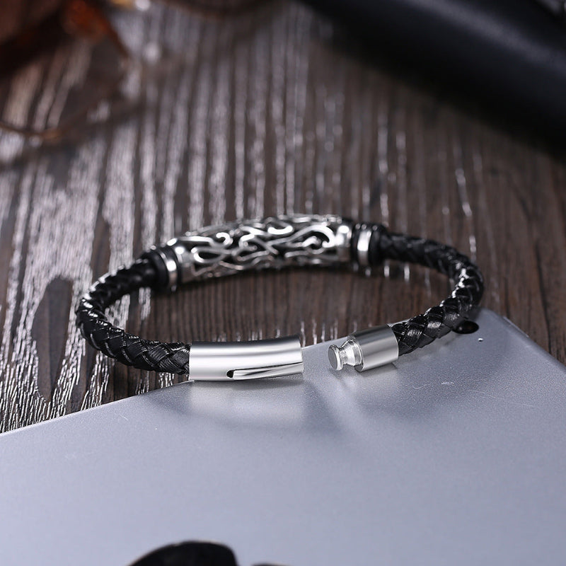 Black braided leather bracelet with silver metal clasp on a wooden surface