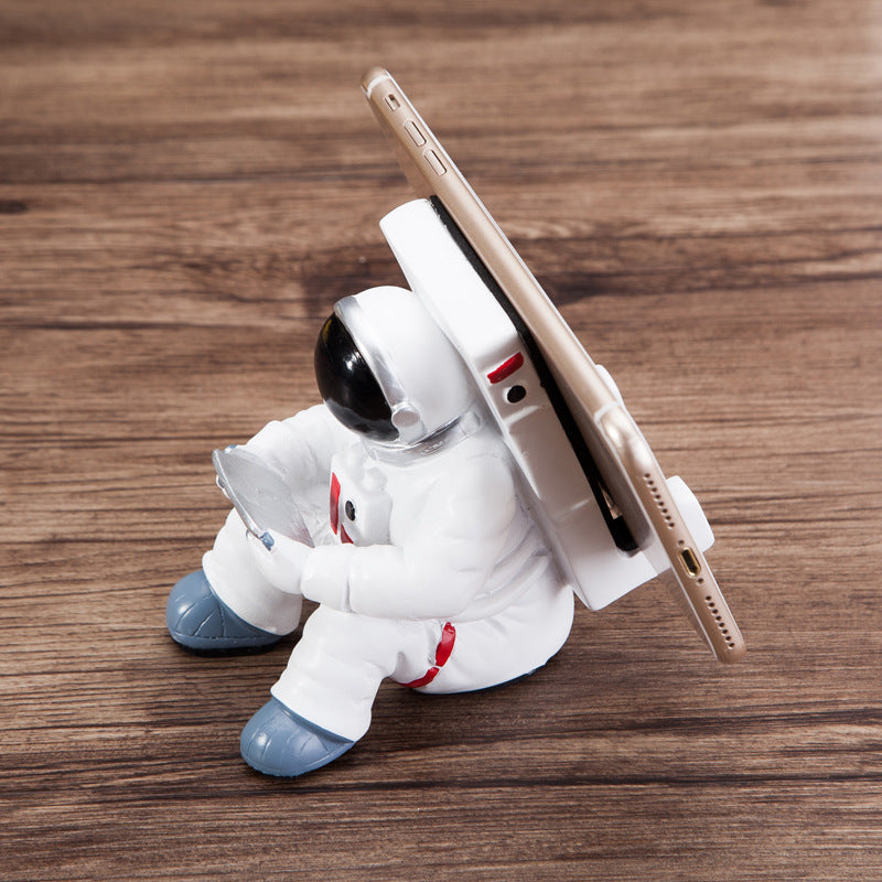 Astronaut mobile phone stand tilted with phone held vertically, white suit and blue boots
