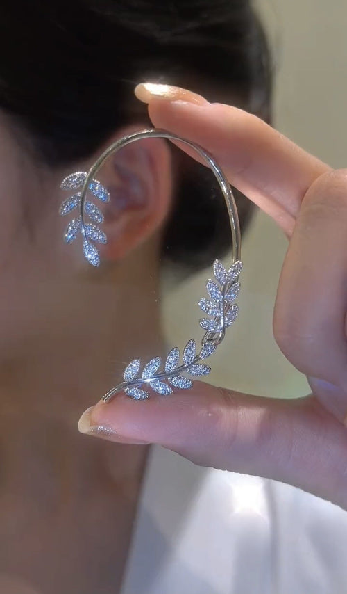 Close-up of a hand holding a silver leaf-shaped earring.