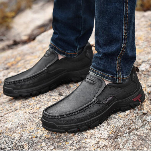 Black slip-on shoes worn with blue jeans on a rocky surface