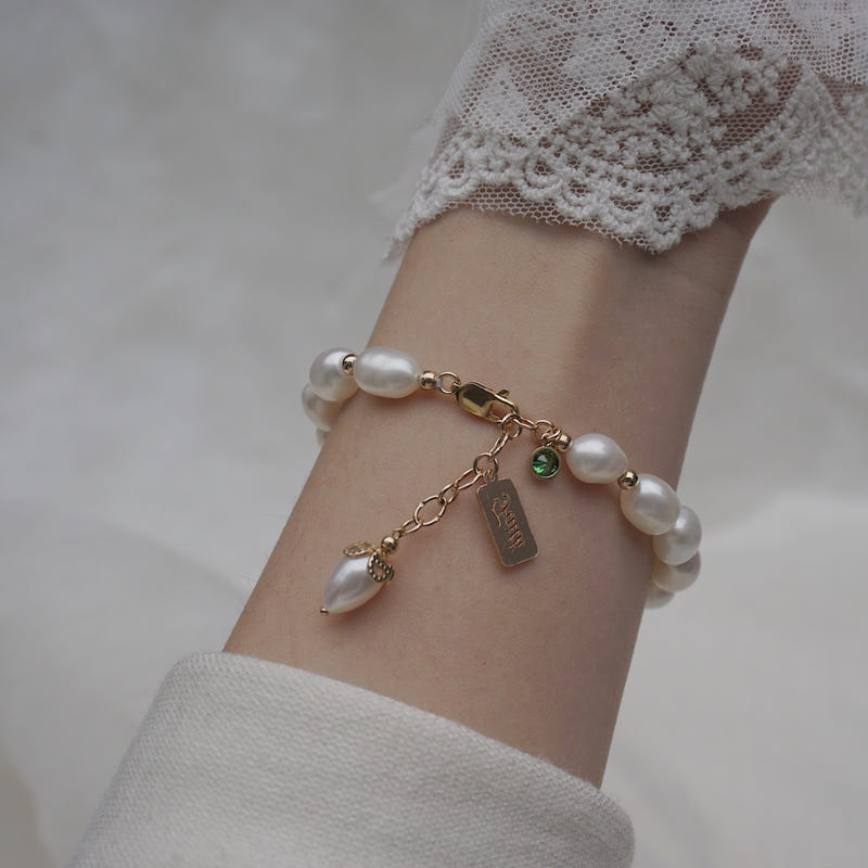Gold-tone pearl bracelet with chain, green zircon charm, and small tag charm
