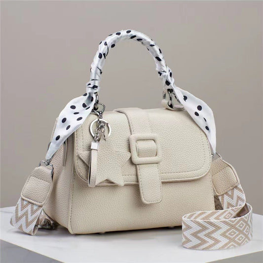 Beige handbag with a polka dot handle and patterned strap on a neutral background