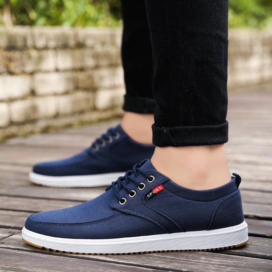 Navy blue casual shoes with white soles worn by a person on a wooden floor.