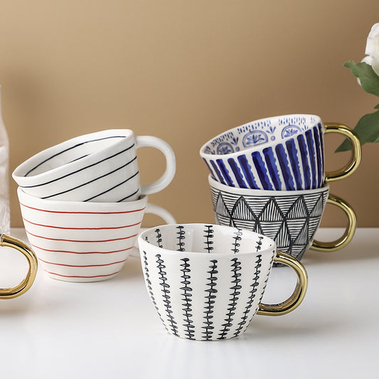 Set of patterned mugs with gold handles on a reflective surface.