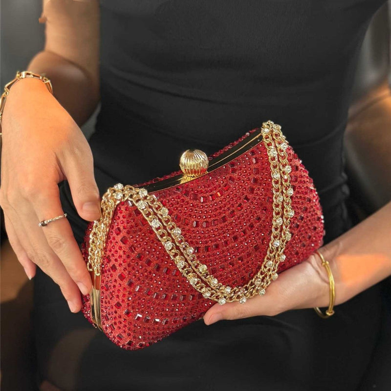 Red handbag with gold chain handle held by a person wearing a black outfit.