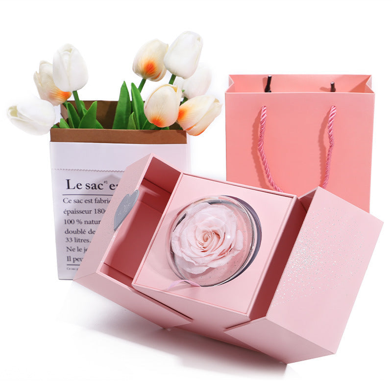 Pink gift box open with clear dome rose and white flower stems in front compartment