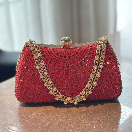 Red handbag with gold chain handle on a reflective surface