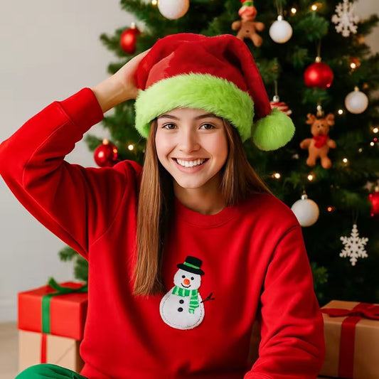 Person wearing a red sweater with a snowman design and a Santa hat in front of a decorated Christmas tree.
