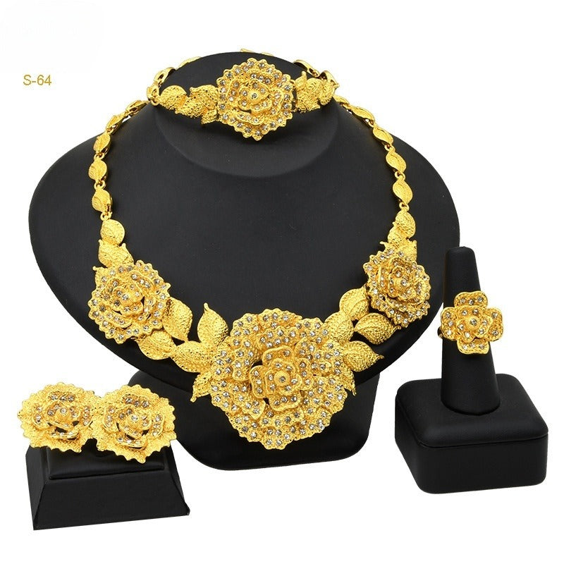 Gold-tone four-piece jewelry set with ornate floral necklace, matching earrings, bracelet, and ring