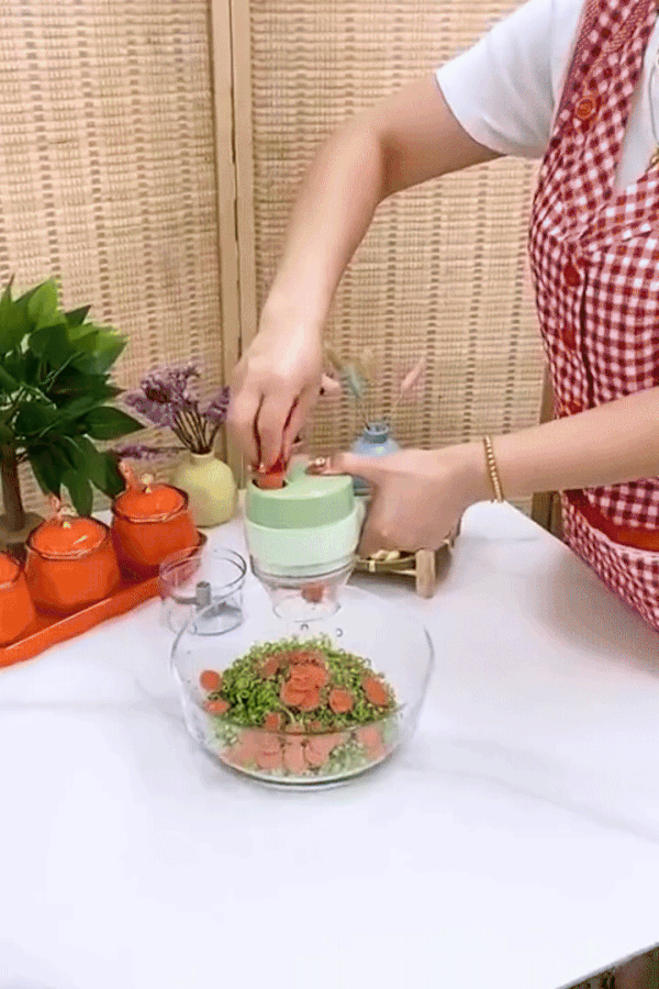Green mini food chopper on a table, chopping herbs with small transparent container