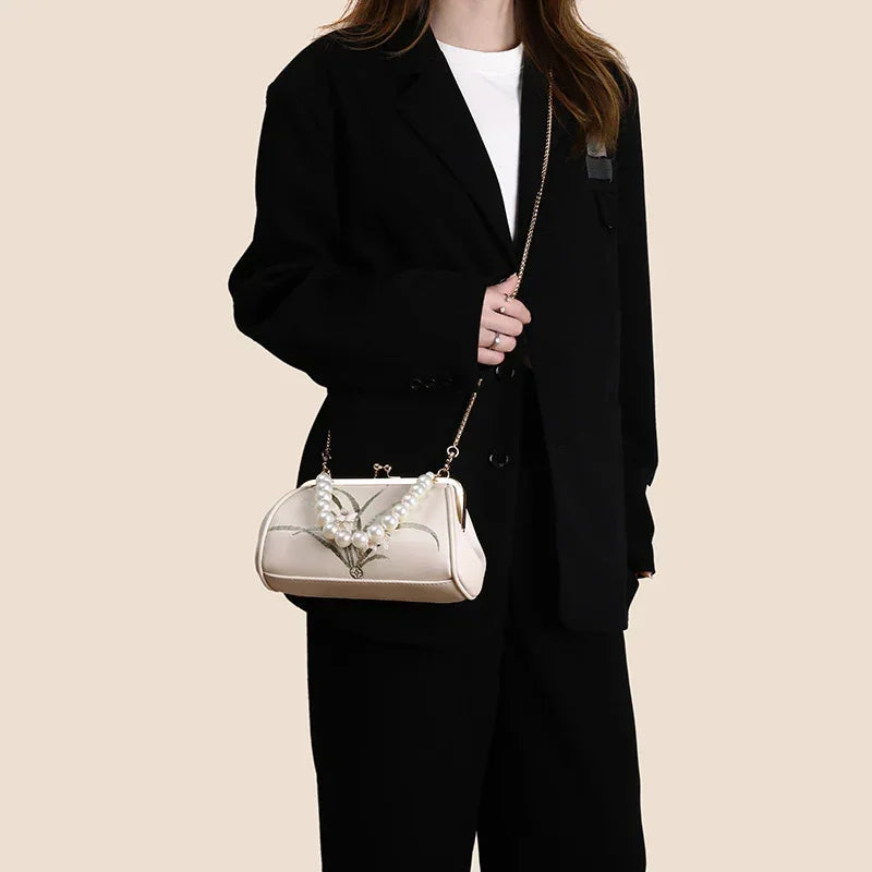 Beige embroidered shoulder bag worn across body with gold chain and pearl handle