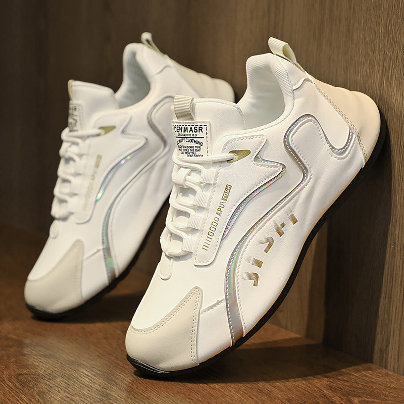 White lace-up sneakers with gold trim and embossed side details, shown on wood