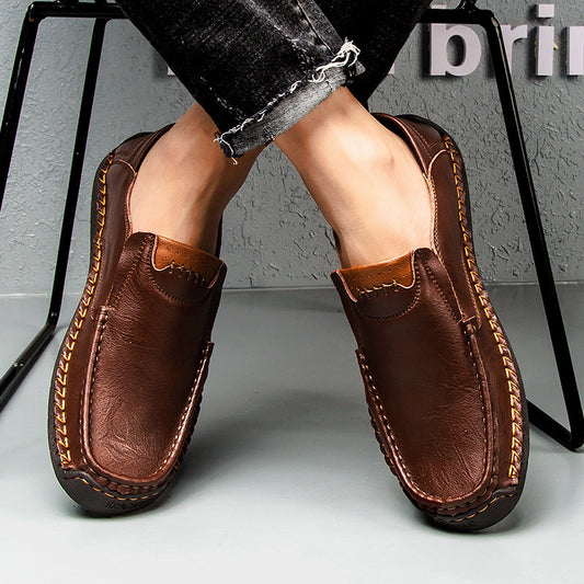 Brown leather loafers worn with black pants on a light gray surface.