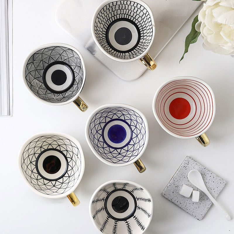 Ceramic mug set with circular eye motifs in black and blue, gold handles