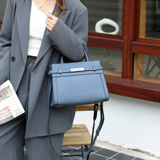 Person in a gray suit holding a blue handbag with a blurred background