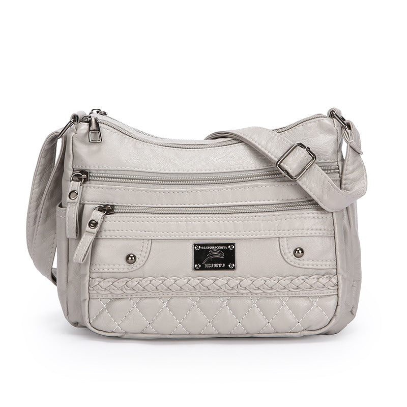 White soft leather shoulder bag with braided front trim, zip pockets, and adjustable buckle strap