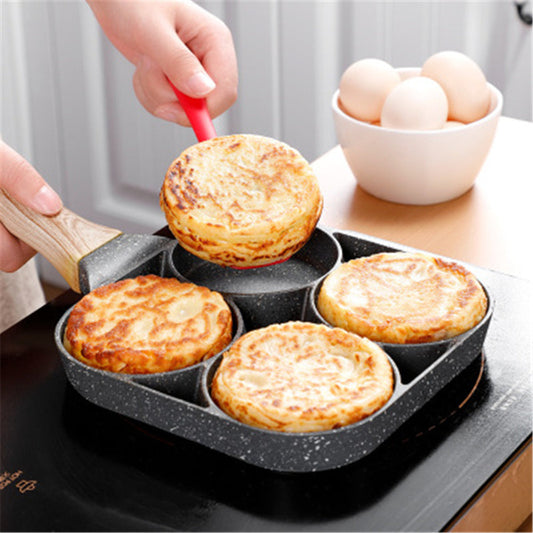 Person using a frying pan with six round compartments to cook small pies or pancakes, with a bowl of eggs in the background.