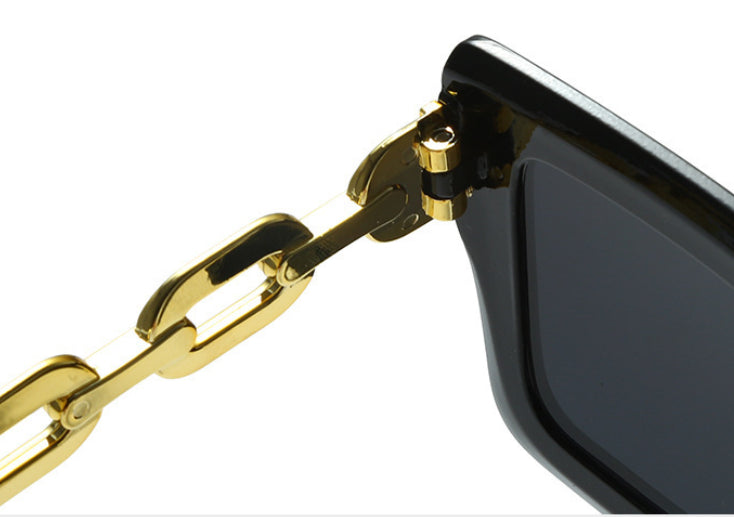 Close-up of square sunglasses hinge with black frame and gold chain hardware.