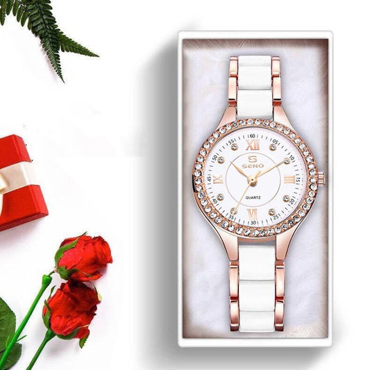 Watch with rose gold and white strap in a box, surrounded by red roses and a red gift bag on a white background.