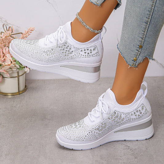 White sneakers with decorative patterns worn by a person on a light gray surface.