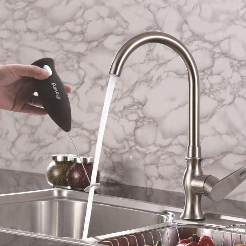 Black electric milk frother held under running water for rinsing.