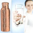 Hammered copper bottle shown beside a glass of water