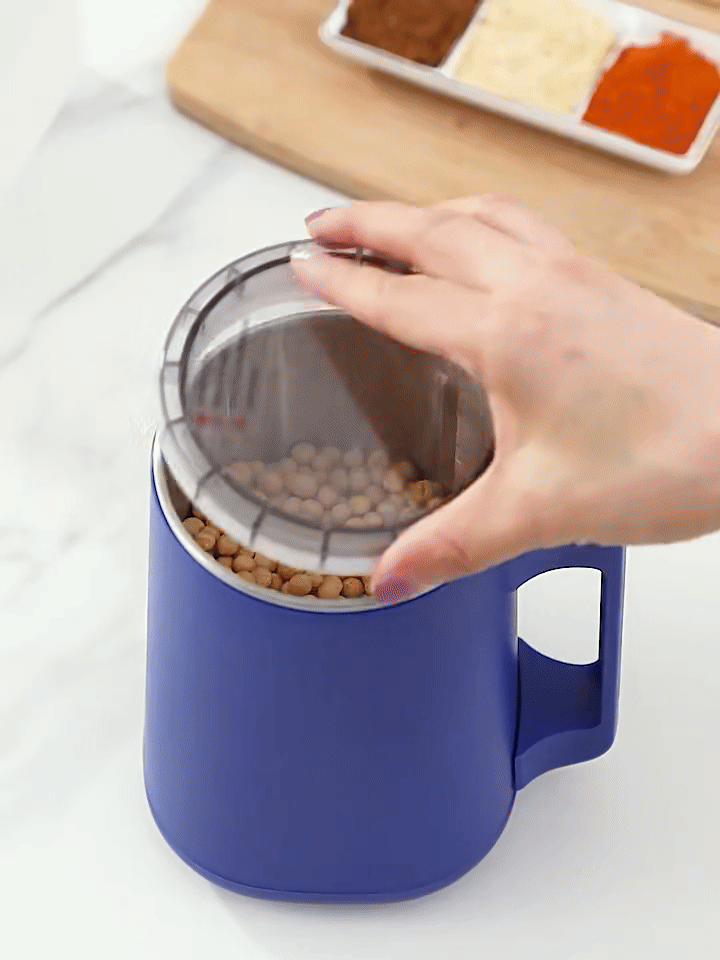 Navy electric grinder filled with coffee beans as its clear lid is closed