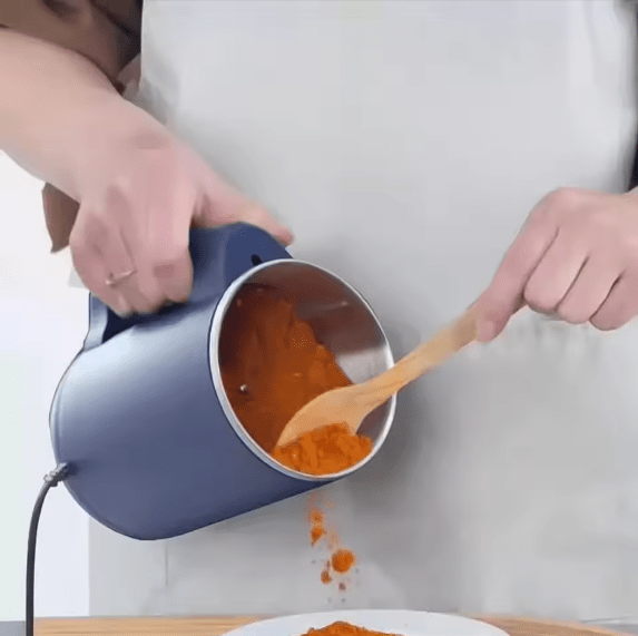 Navy electric grinder tipped to pour ground coffee with a wooden spoon