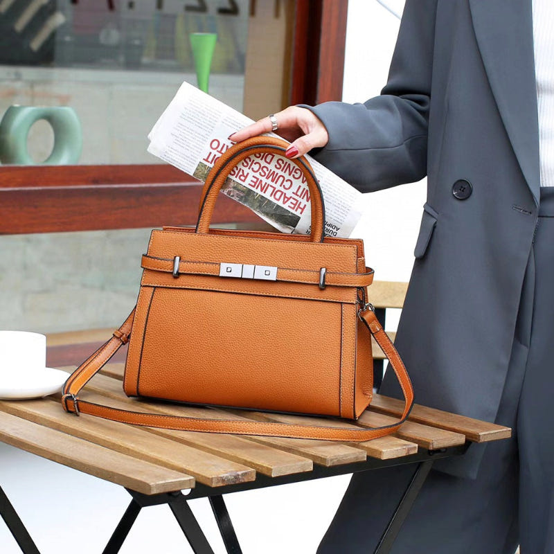 Cognac small square genuine leather shoulder bag with top handle and front buckle detail.