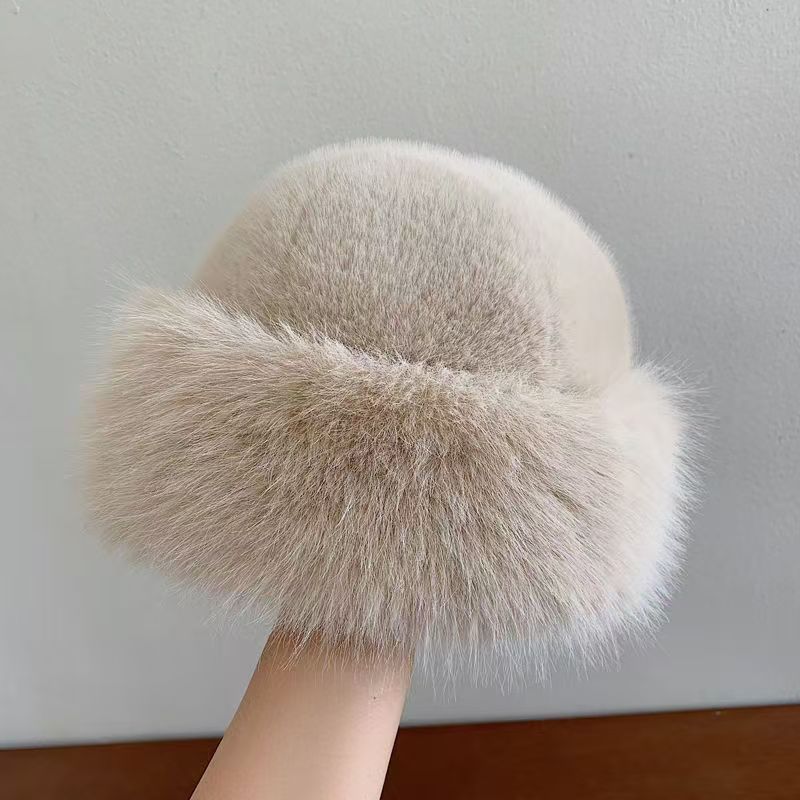 Beige fur pom-pom held by a hand against a neutral background