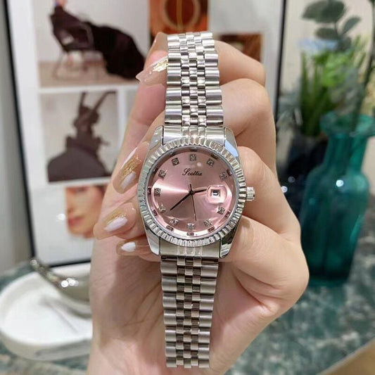 Hand holding a silver watch with a pink face against a blurred indoor background