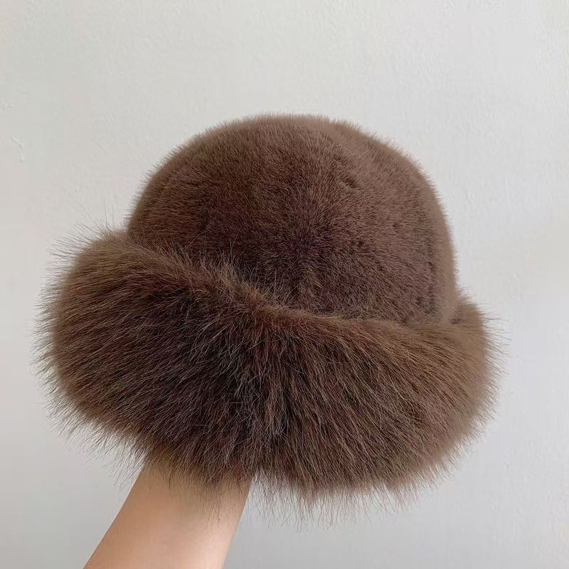 Brown fur hat held by a hand against a light gray background