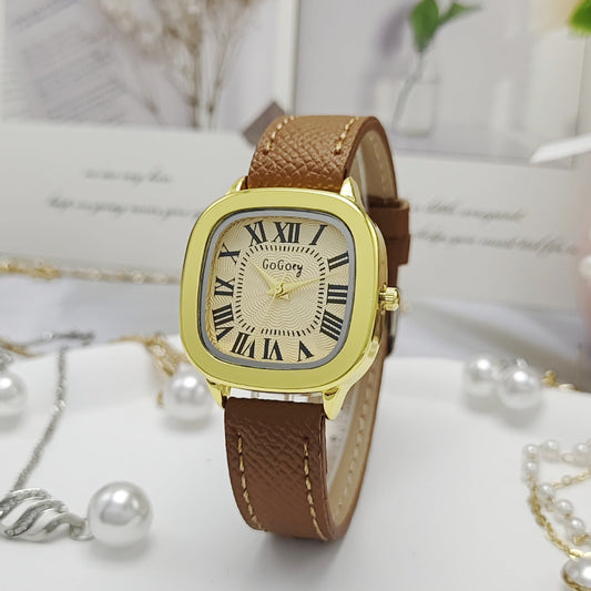 Gold watch with brown leather strap on a white surface with pearls and jewelry.