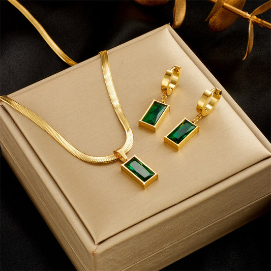 Gold necklace and earrings with green gemstones on a beige jewelry box.