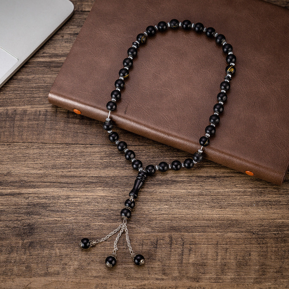 Men's black beaded bracelet necklace with tassel, resting on brown leather notebook.