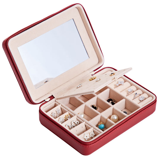 Red jewelry box with mirror lid containing various jewelry items on a white background