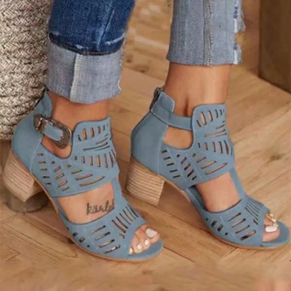 Blue cut-out high-heeled shoes worn with rolled-up jeans on a wooden floor.