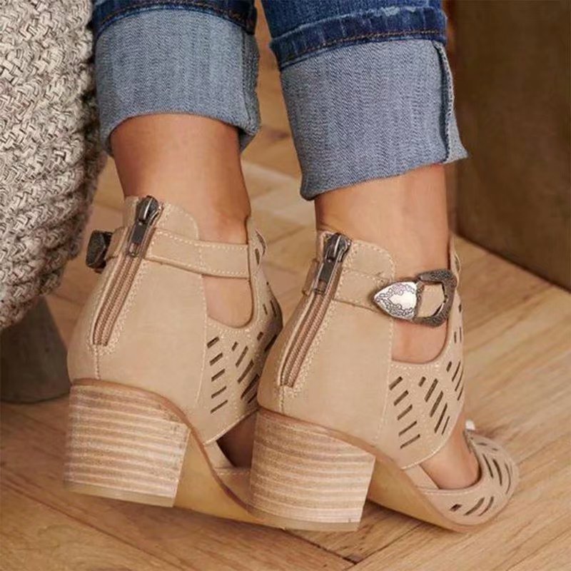 Beige high-heeled shoes with cut-out design worn by a person on a wooden floor.