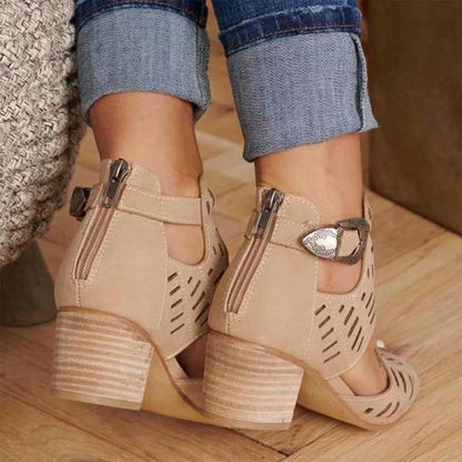 Beige high-heeled shoes with cut-out design worn by a person on a wooden floor.