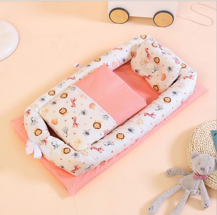 Baby nest with white animal print sides, pink inner padding, and two pillows