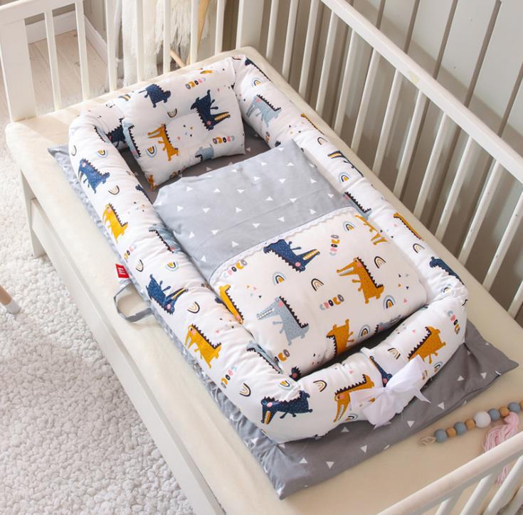 Portable baby nest crib with white dinosaur print mattress and two bolster pillows