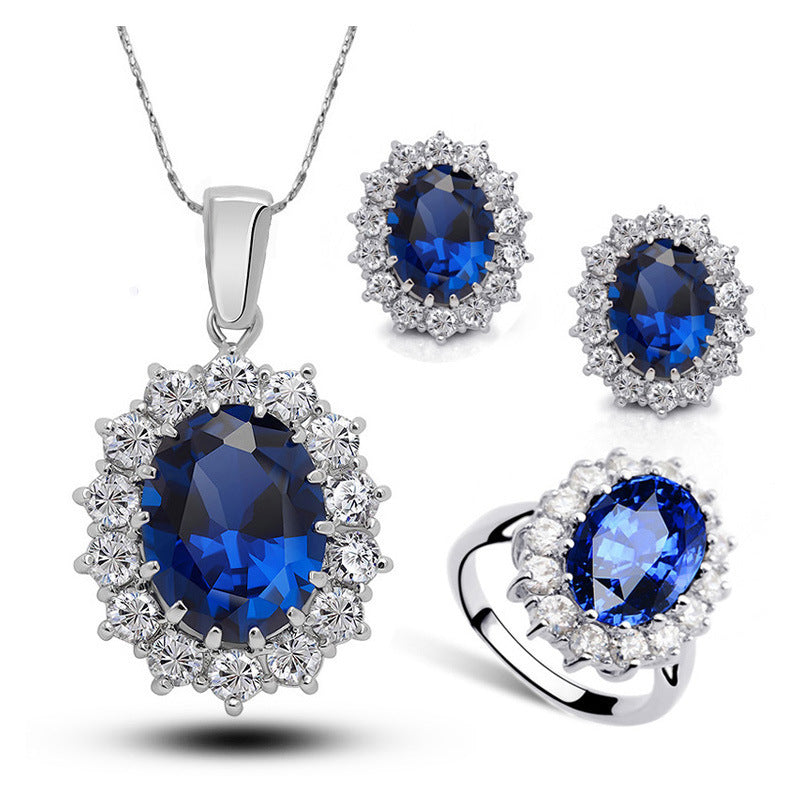 Crystal bridal jewelry set with sapphire-blue round halo stones on necklace, earrings, and ring.